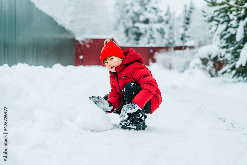 A boy in a red jacket and a red hat screams and laughs in the snow
