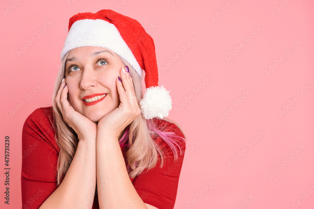 Portrait of a dreaming woman in a red Santa hat on a pink background Portrait of a dreaming woman in a red Santa hat on a pink background