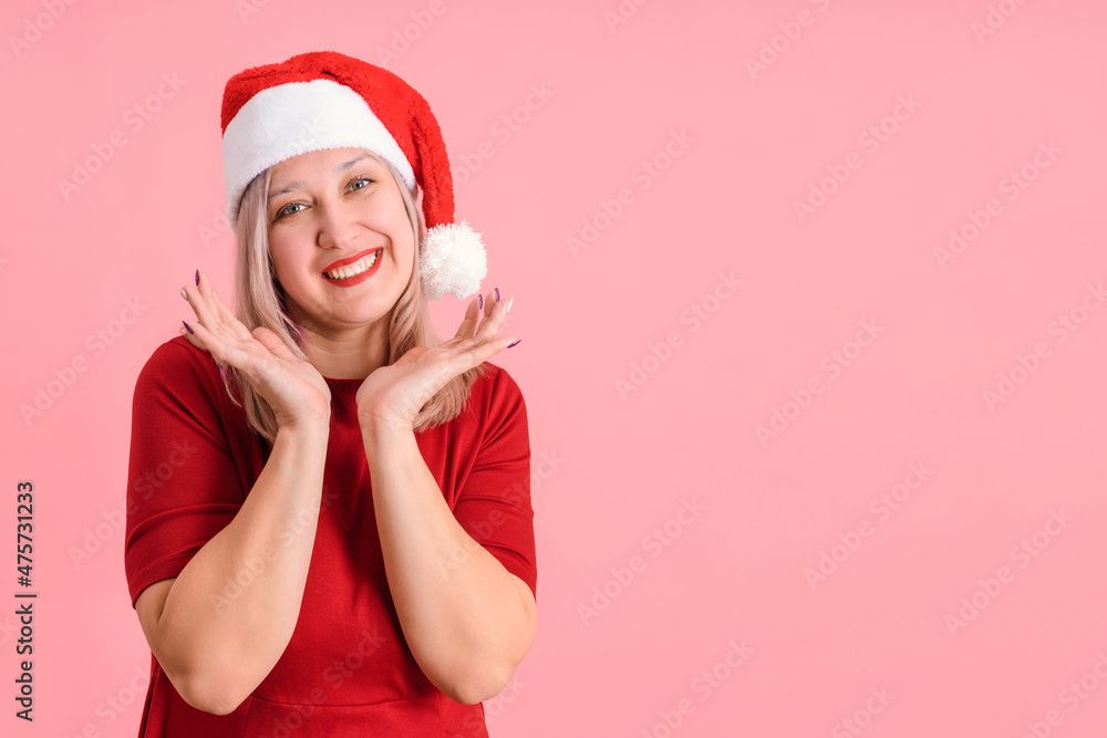 Joyful 40s woman in santa hat on pink background, copyspace