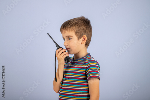 The boy is talking on the radio. A professional walkie-talkie in the child's hand. The child speaks into a walkie-talkie on a blue background.