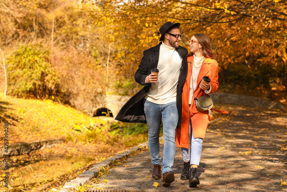 Obraz premium Loving couple holding paper cups with drink and walking in autumn park