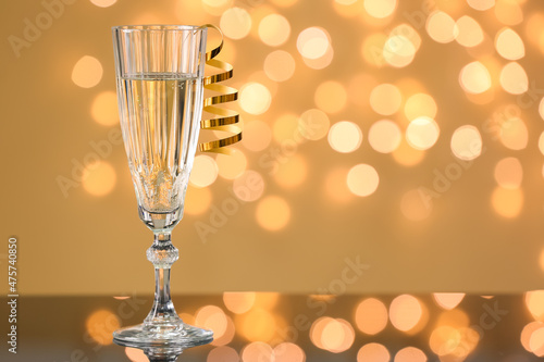 Glass of champagne with serpentine on table against blurred lights photo