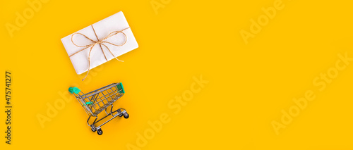 Christmas composition eco crafted gift box and shopping cart. Sale, shopping, black friday, cyber monday, New year concept, top view, flat lay, isolated, copy space on minimal yellow background