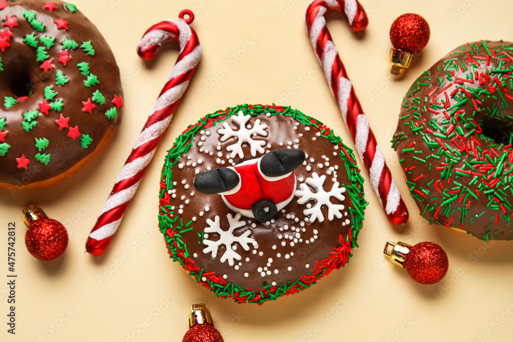 Tasty Christmas donuts with balls and candy canes on beige background