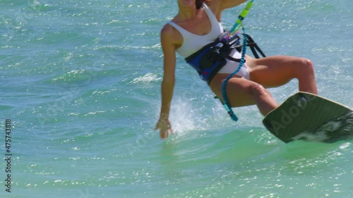 A beautiful young girl in a white swimsuit rides the waves on a kite on a clean and transparent ocean