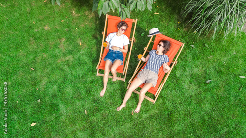 Fotografia Young girls relax in summer garden in sunbed deckchairs on grass, women friends
