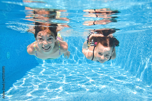 Children swim in swimming pool underwater, little active girls have fun under water, kids fitness and sport on family vacation