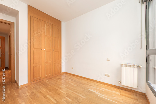 Empty bedroom with built-in wardrobe, oak parquet flooring and white aluminum radiators