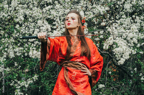 Young girl in traditional kimano in a blooming garden with samurai japanese sword katana in image of warrior woman
