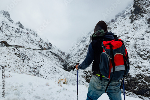 Unrecognizable man from behind with red backpack hiking in a snowy mountain landscape.