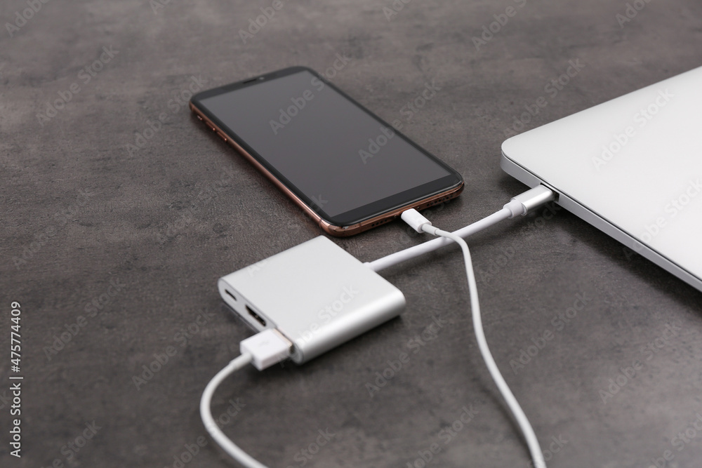 Modern smartphone and laptop charging from power bank on grey table, closeup Modern smartphone and laptop charging from power bank on grey table, closeup