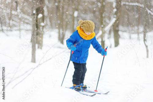 Cute little boy is learning ski during walk in the winter forest. Outdoor activities for children in winter. Kids equipment for winter sports.