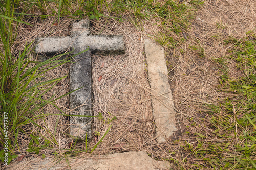 A old concrete cross in the ground marks an unmarked grave or burial site under the ground. At a public cemetery at the Philippines.