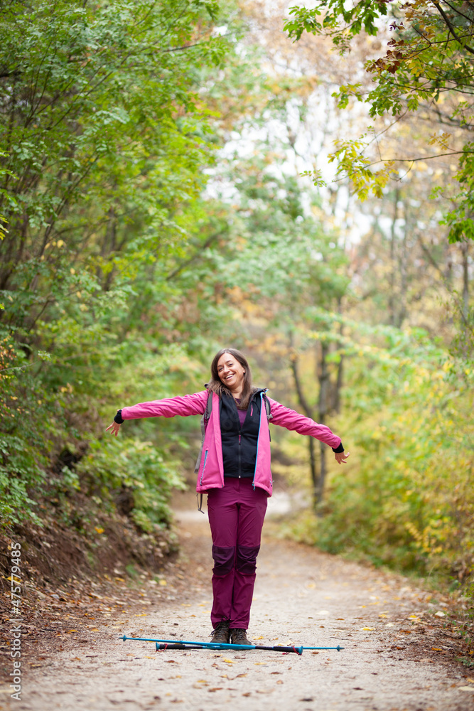Hiker girl standing on a wide trail in the mountains. Backpacker with pink jacket in a forest. Healthy fitness lifestyle outdoors. Hiker girl standing on a wide trail in the mountains. Backpacker with pink jacket in a forest. Healthy fitness lifestyle outdoors.