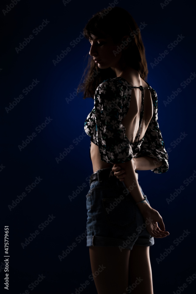Half silhouette portait of a beautiful young girl on dark blue background.