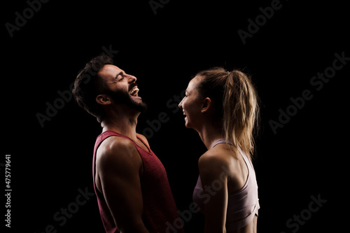 Fit couple posing together. Boy and girl side lit silhouettes on black background.