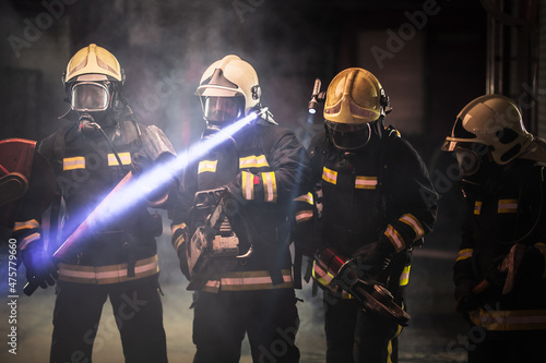 Fototapeta Group of professional firefighters wearing full equipment, oxygen masks, and emergency rescue tools, circular hydraulic and gas saw, axe, and sledge hammer