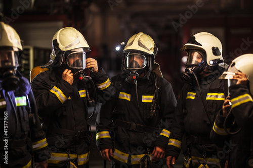 Group of professional firefighters. Firemen wearing uniforms, protective helmets and oxygen masks. Smoke in the background.