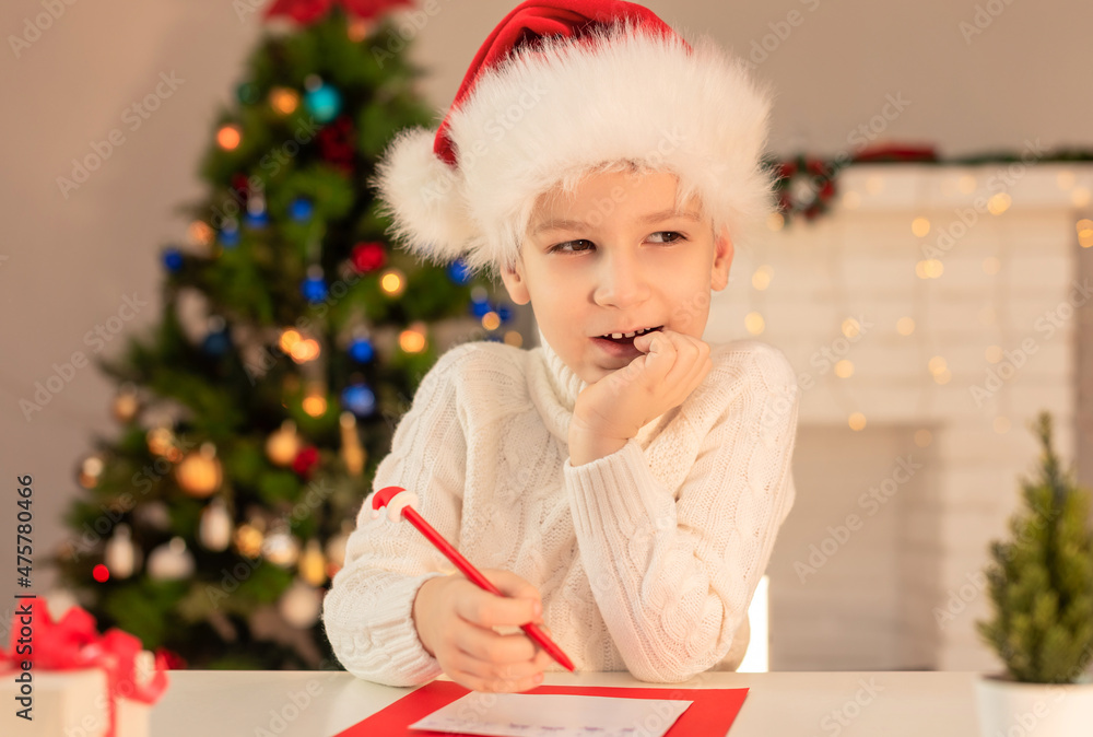 Child boy in red Santa hat writing a letter to Santa Claus. Christmas or New Year cozy holidays concept. Xmas time. Selective focus Child boy in red Santa hat writing a letter to Santa Claus. Christmas or New Year cozy holidays concept. Xmas time. Selective focus