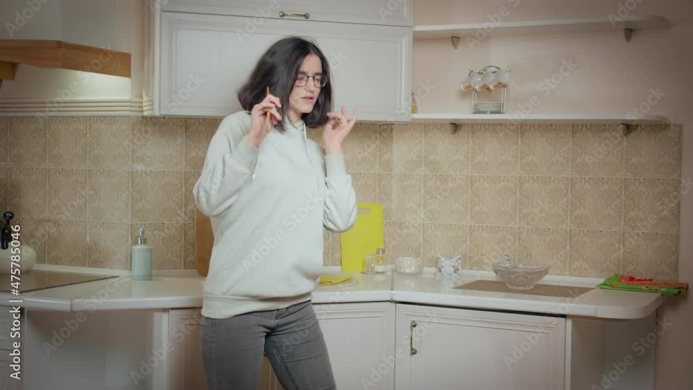Girl is having fun on the background of the kitchen at home, holding a wooden spoon and singing Girl is having fun on the background of the kitchen at home, holding a wooden spoon and singing
