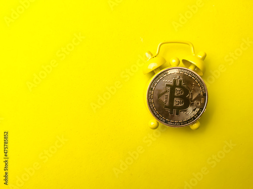 Bitcoin and alarm clock on a yellow background with copy space for text and design.