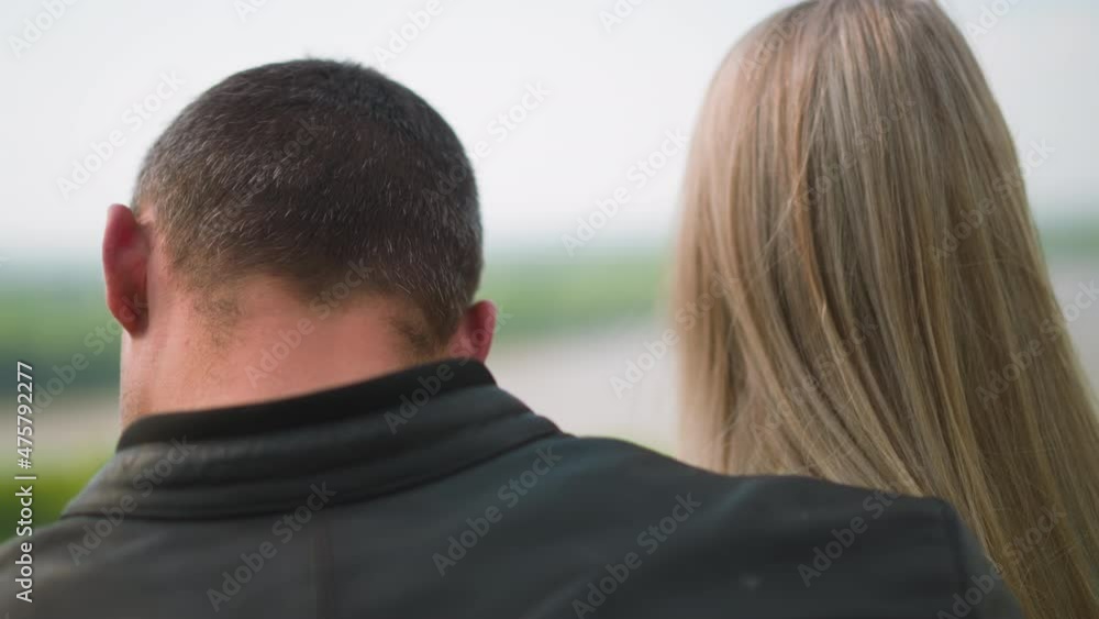 Guy in black leather clothes hugs long fair haired lady standing against picturesque lake on summer day close backside view slow motion Guy in black leather clothes hugs long fair haired lady standing against picturesque lake on summer day close backside view slow motion