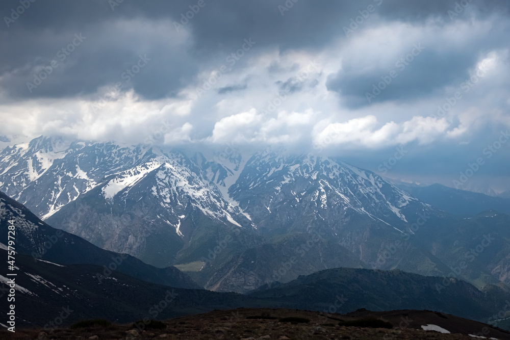 Rocky mountains covered with snow with storm clouds on background. Rocky mountains covered with snow with storm clouds on background.