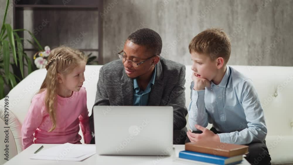 African-American English native speaker tutor gives task to brother and younger sister students at laptop computer in living room slow motion