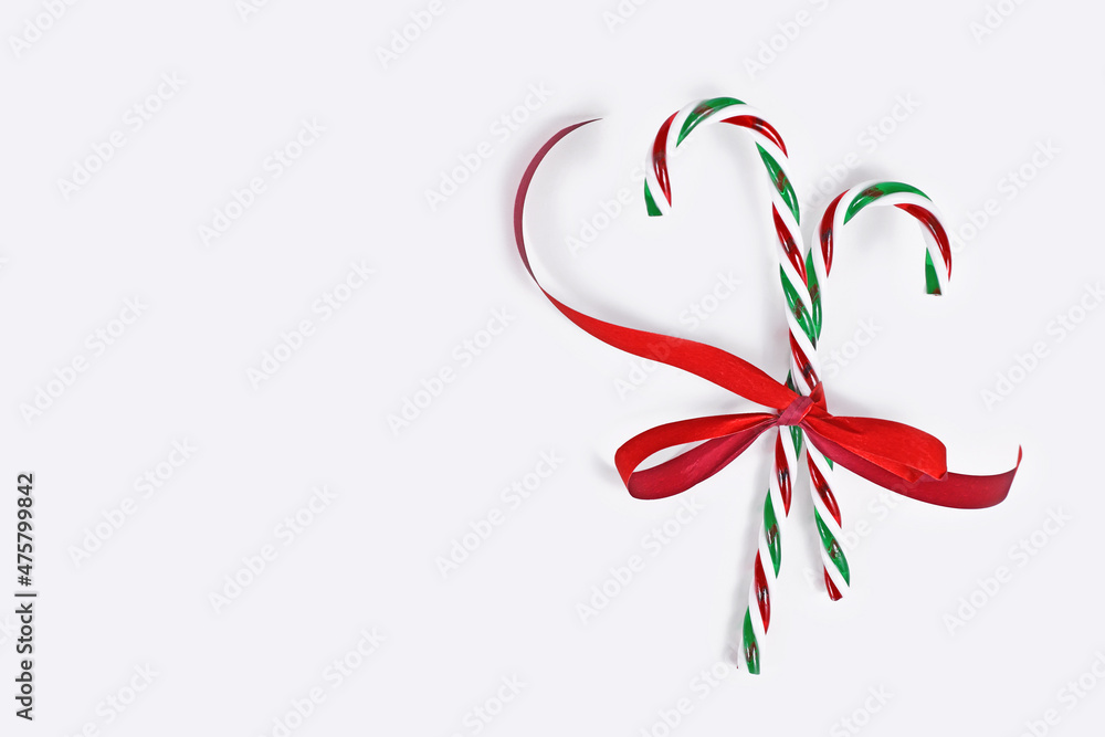 Striped candy canes tied together with red ribbon on side of white background with copy space Striped candy canes tied together with red ribbon on side of white background with copy space