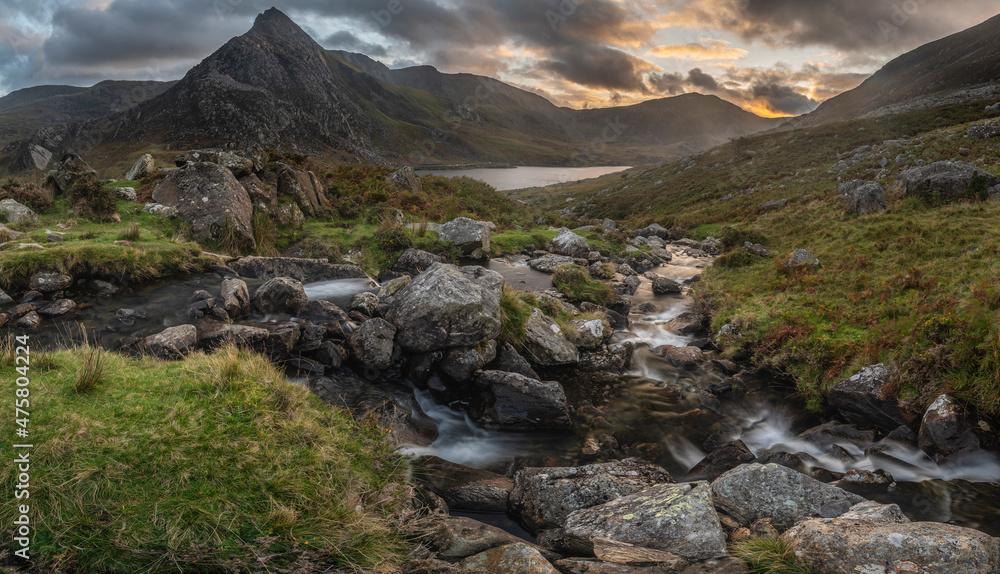 Epic moody Autumn sunset landscape image of Llyn Ogwen and Tryfan in Snowdonia National Park with stream and rocks in foreground Epic moody Autumn sunset landscape image of Llyn Ogwen and Tryfan in Snowdonia National Park with stream and rocks in foreground