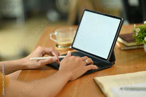 Cropped image of a young freelance man using a white blank screen digital tablet and stylus pen at the wooden working desk.
