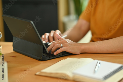 Cropped image of a young freelance man using a digital tablet and stylus pen at the wooden working desk.