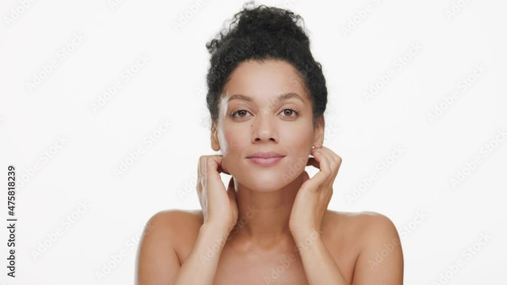 Close-up beauty portrait of young beautiful slim African American woman with black curly hair in bun moves head up stroking neck and smiling for the camera on white background | Skin care concept Close-up beauty portrait of young beautiful slim African American woman with black curly hair in bun moves head up stroking neck and smiling for the camera on white background | Skin care concept