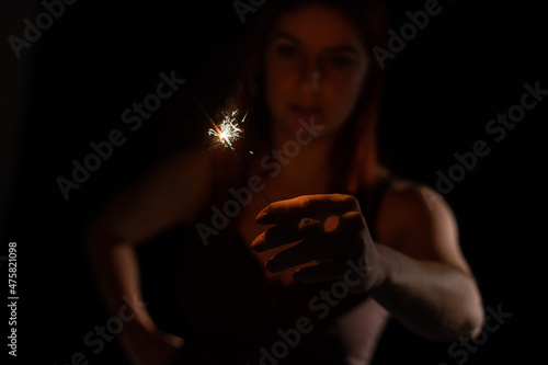 Caucasian woman holding sparkler in the dark.