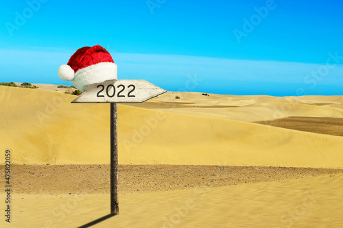 2022, a wooden sign in a Santa Claus Hat on a background of sand dunes. New Year card. .