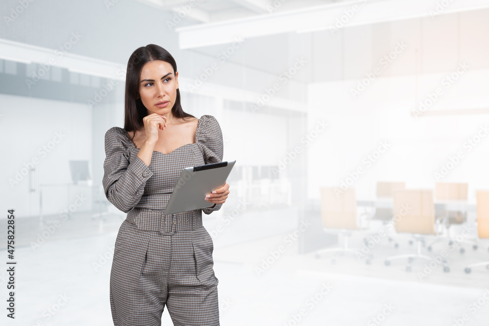 Businesswoman with tablet in hands, pensive look on background of office room Businesswoman with tablet in hands, pensive look on background of office room