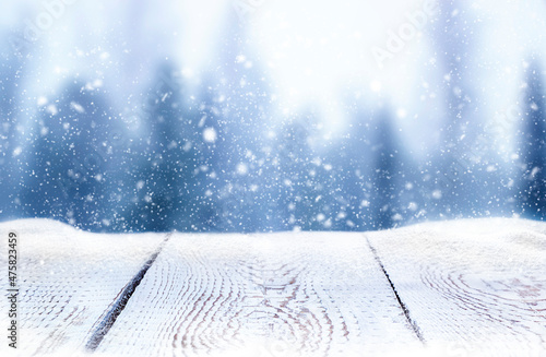 white wooden table in snow on blurred forest background in snowfall © Алена Ягупа