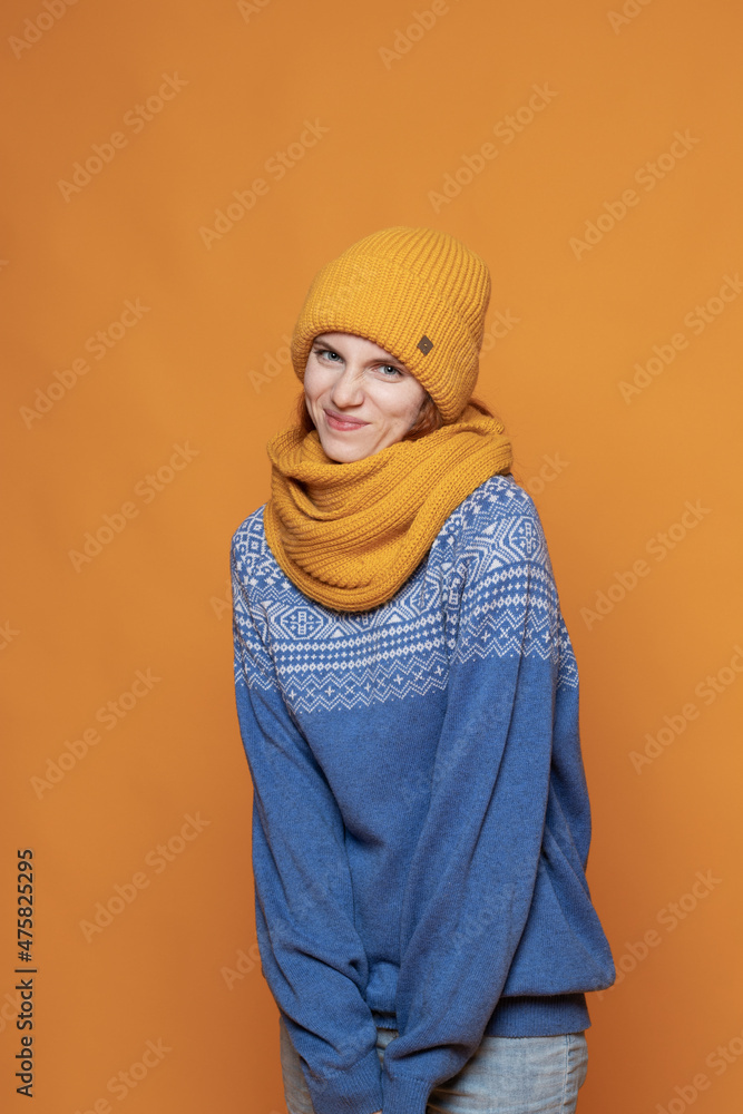 young red-haired girl in a warm hat and a knitted sweater on a yellow background young red-haired girl in a warm hat and a knitted sweater on a yellow background