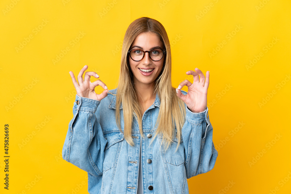 Young blonde woman isolated on yellow background showing ok sign with two hands
