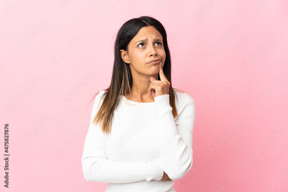 Obraz premium Caucasian girl isolated on pink background having doubts while looking up