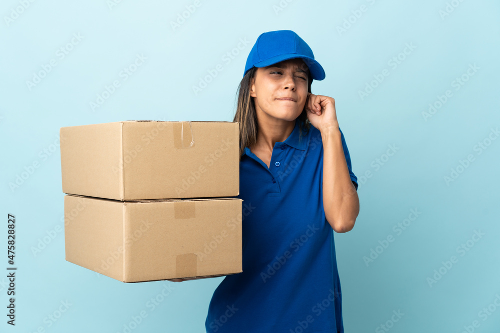 Young delivery woman isolated on blue background frustrated and covering ears Young delivery woman isolated on blue background frustrated and covering ears