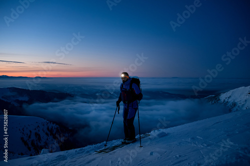 male tourist skier with a flashlight on his forehead against the backdrop of picturesque evening sky