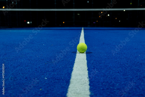 Fotografía A paddle tennis ball in the foreground on the line of a blue paddle tennis court at night