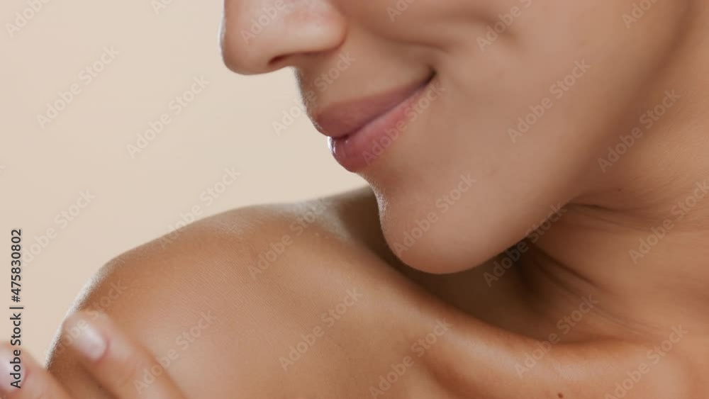 Horizontal extreme close-up of good-looking slim woman strokes her shoulder smiling on beige background | Skin nourishing concept Horizontal extreme close-up of good-looking slim woman strokes her shoulder smiling on beige background | Skin nourishing concept