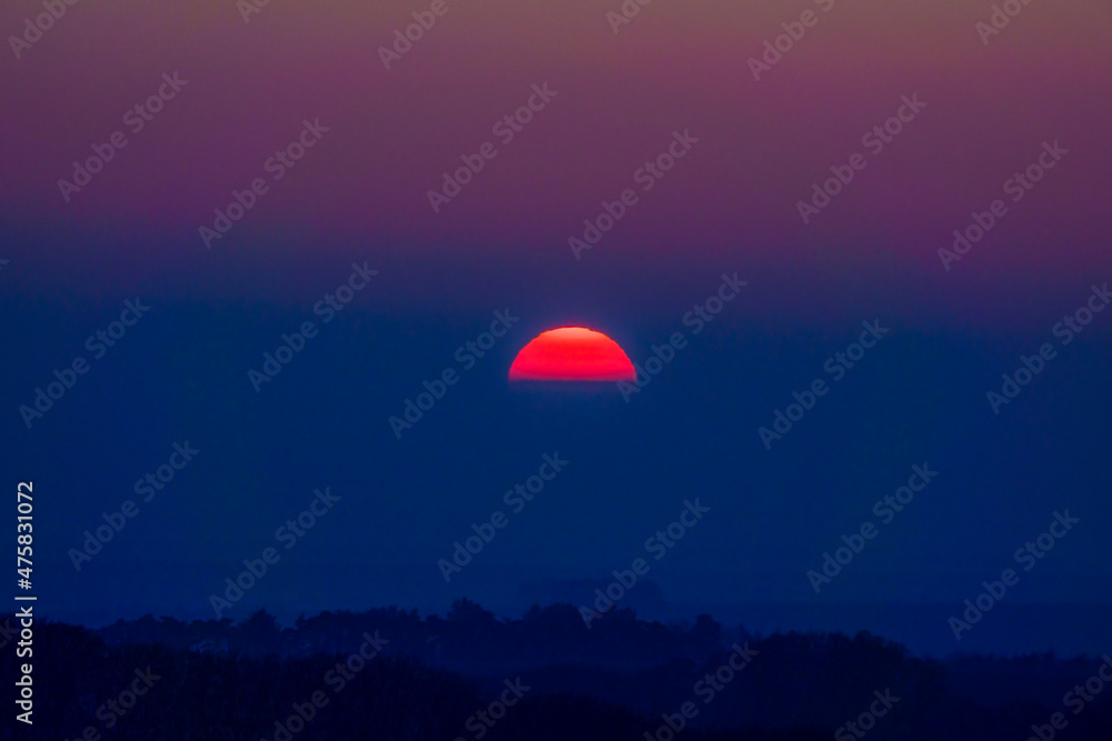 dramatic sky as the sun sets through low cloud with a glowing red golden silhouette, Wiltshire UK dramatic sky as the sun sets through low cloud with a glowing red golden silhouette, Wiltshire UK
