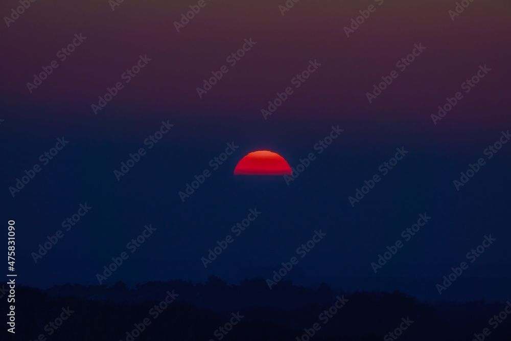 dramatic sky as the sun sets through low cloud with a glowing red golden silhouette, Wiltshire UK dramatic sky as the sun sets through low cloud with a glowing red golden silhouette, Wiltshire UK