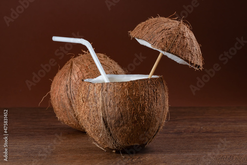 Coconut cocktail with a straw on brown background.