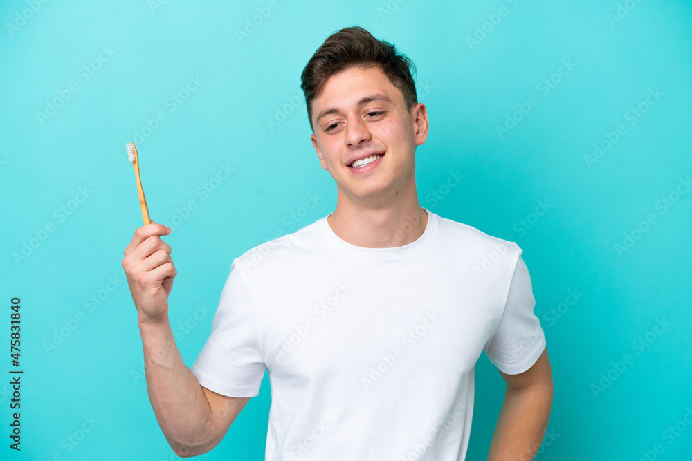 Young Brazilian man brushing teeth isolated on blue background posing with arms at hip and smiling Young Brazilian man brushing teeth isolated on blue background posing with arms at hip and smiling