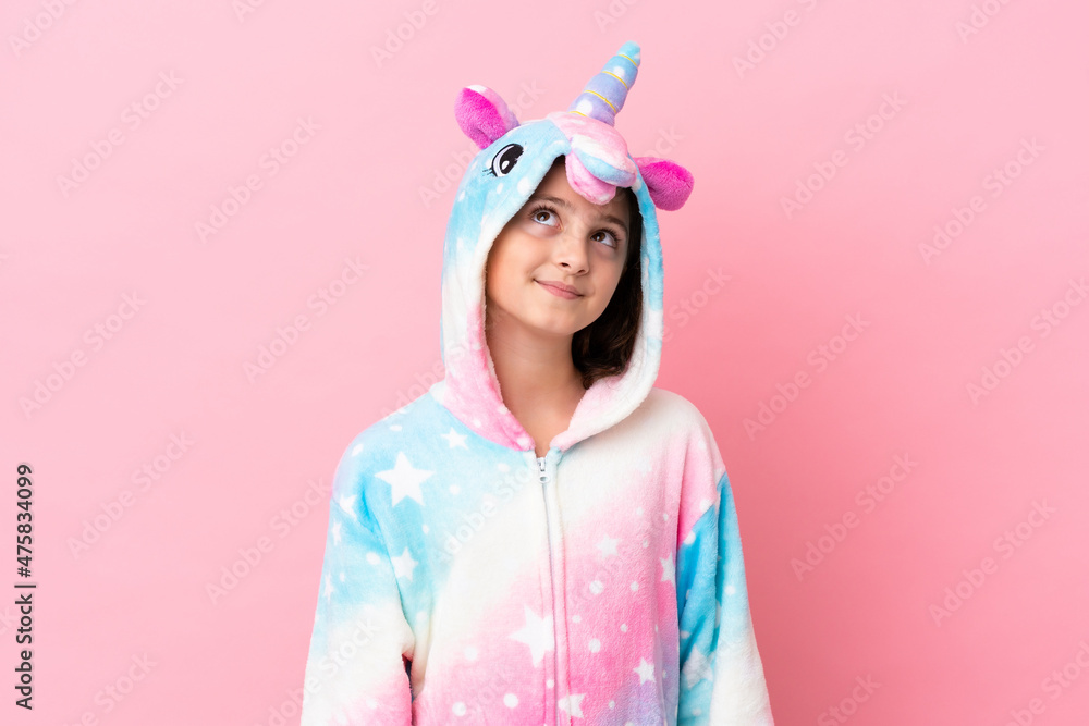 Little caucasian woman wearing a unicorn pajama isolated on pink background thinking an idea while looking up