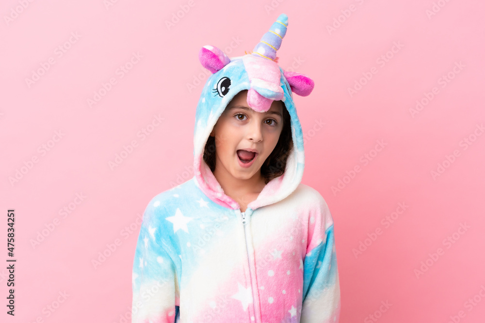 Little caucasian woman wearing a unicorn pajama isolated on pink background with surprise facial expression